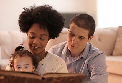 A couple at home with their daughter reading a book.